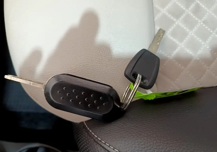 Gros plan sur deux clés noires posées sur un siège en cuir blanc et noir, sans vue du véhicule.