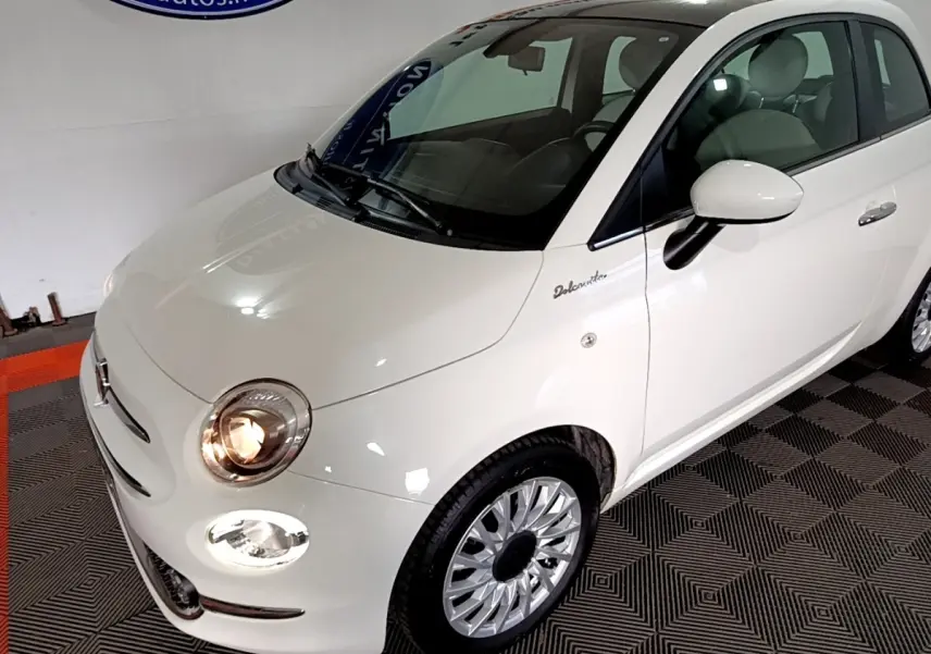 Vue 3/4 avant droite de la Fiat 500 Dolcevita blanche avec phares allumés et jantes alliage distinctives.