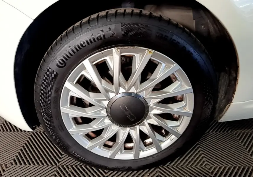 Gros plan sur la roue avant droite blanche d'une Fiat 500 Hybrid avec jante argentée au design étoilé.