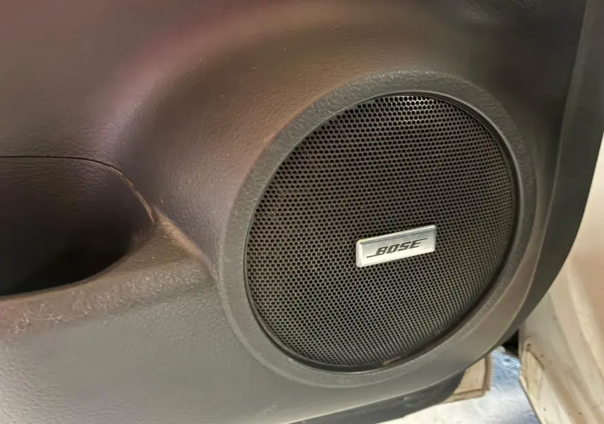 Gros plan sur l'enceinte Bose intégrée à la porte intérieure noire d'un Nissan Qashqai blanc, version Tekna+ 2021.