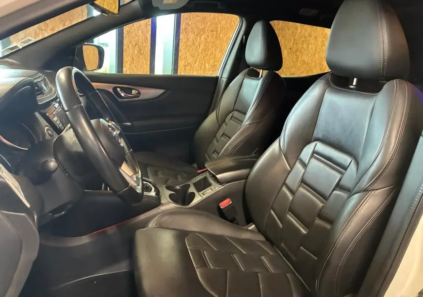 Vue intérieure côté conducteur du Nissan Qashqai blanc 2021, sièges en cuir noir et volant multifonction.