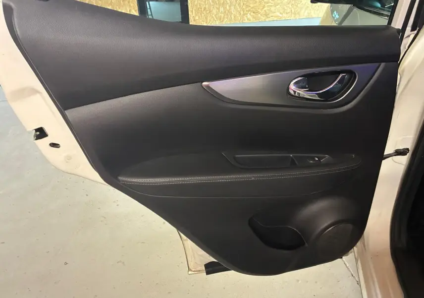 Gros plan sur la porte arrière droite noire en cuir du Nissan Qashqai blanc 2021, avec poignée chromée et bouton de fenêtre.