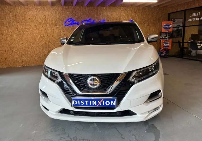Vue frontale d'un Nissan Qashqai blanc 2021 dans un showroom avec logo Distinxion sur la plaque avant.