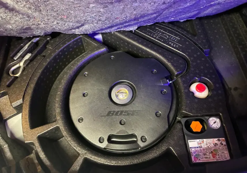 Détail du coffre du Nissan Qashqai blanc 2021 montrant le caisson Bose intégré et les outils de secours.