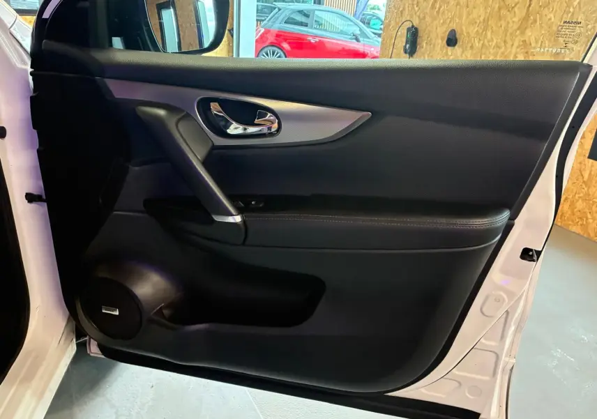 Vue intérieure de la porte avant gauche blanche du Nissan Qashqai 1.5 BlueDCI Tekna+ avec garniture noire et poignée chromée.