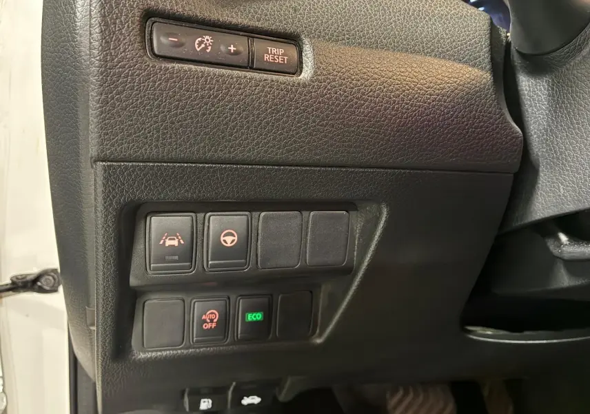 Détail des commandes côté gauche du tableau de bord noir du Nissan Qashqai blanc, avec boutons d'assistance et mode ECO.