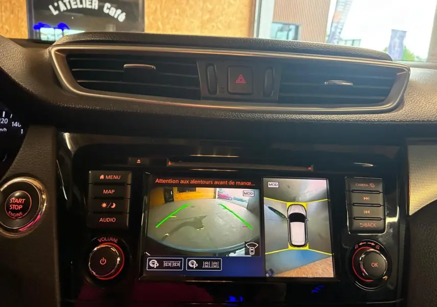 Vue rapprochée de l’écran central du Nissan Qashqai blanc 2021 montrant la caméra de recul et l’alerte de proximité.