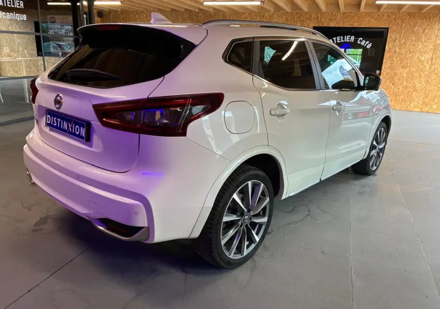 Vue 3/4 arrière droite d'un Nissan Qashqai blanc 2021 avec jantes alliage et vitres teintées, stationné en intérieur.
