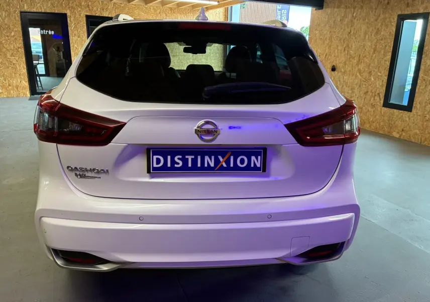 Vue arrière d'un Nissan Qashqai blanc 2021 avec logo et plaque Distinxion dans un garage lumineux.