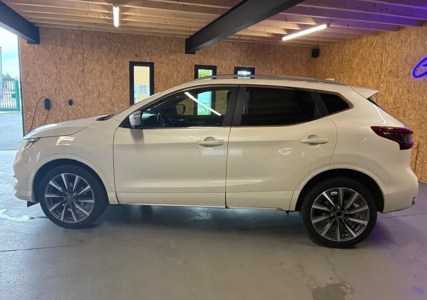Vue de profil côté gauche d'un Nissan Qashqai blanc 2021 stationné en intérieur avec jantes alliage foncé.