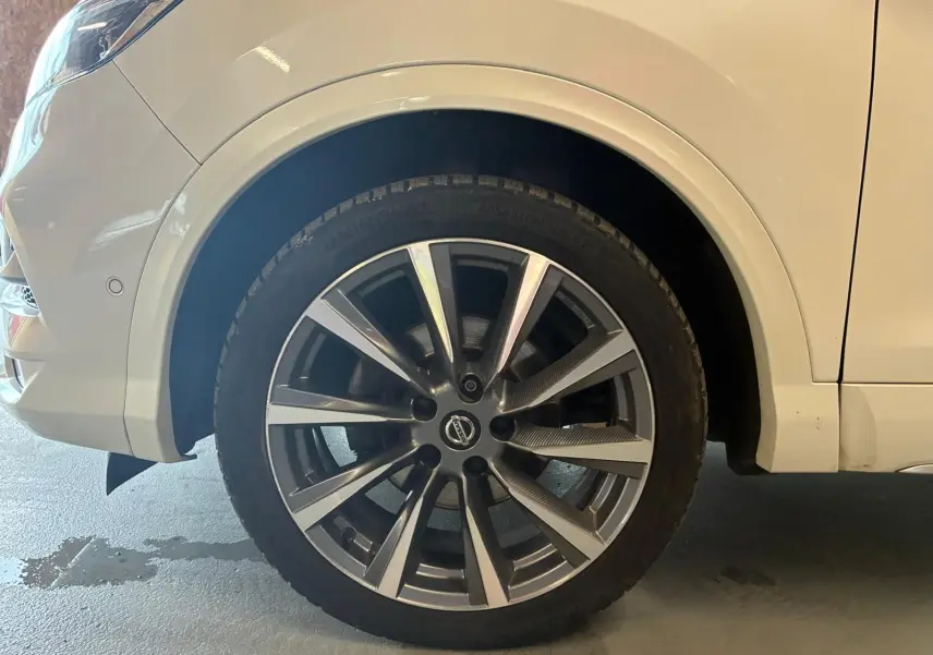 Gros plan sur la roue avant gauche d'un Nissan Qashqai blanc, mettant en valeur la jante alliage moderne.