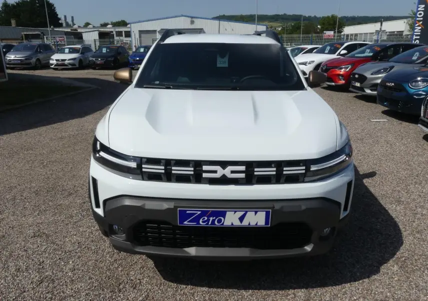 Vue de face d'un Dacia Duster blanc avec calandre noire et détails de bouclier gris foncé sur parking.