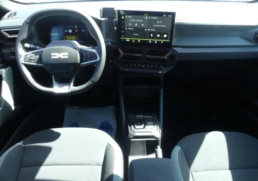 Intérieur du Dacia Duster 2025 en vue frontale, tableau de bord noir avec écran tactile central et volant multifonction.