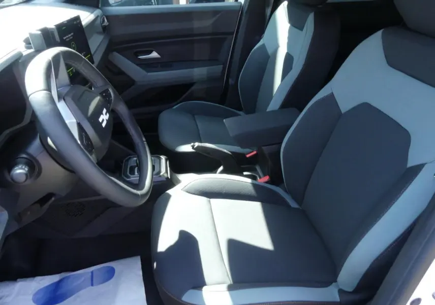 Intérieur avant droit du Dacia Duster 2025, sièges bi-ton gris avec accoudoir central et volant noir.