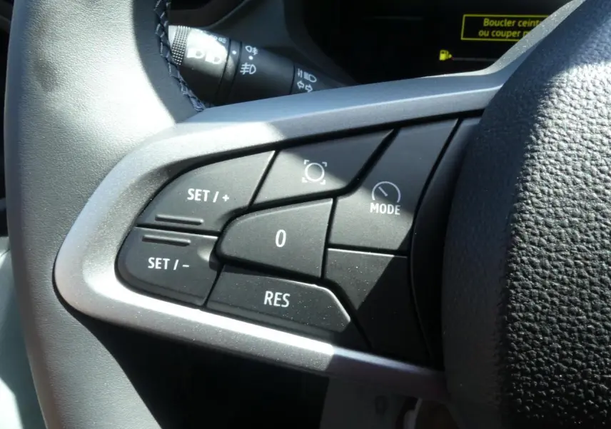 Gros plan sur les commandes de régulateur de vitesse au volant noir du Dacia Duster blanc hybride 2025.