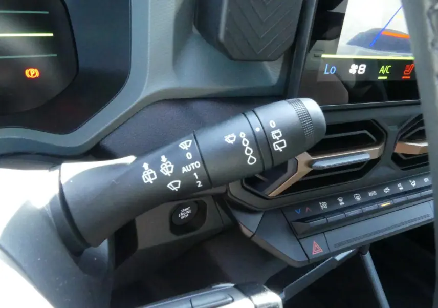 Gros plan sur la commande d'essuie-glace et la console centrale noire avec détails brun cuivré du tableau de bord du Dacia Duster blanc.