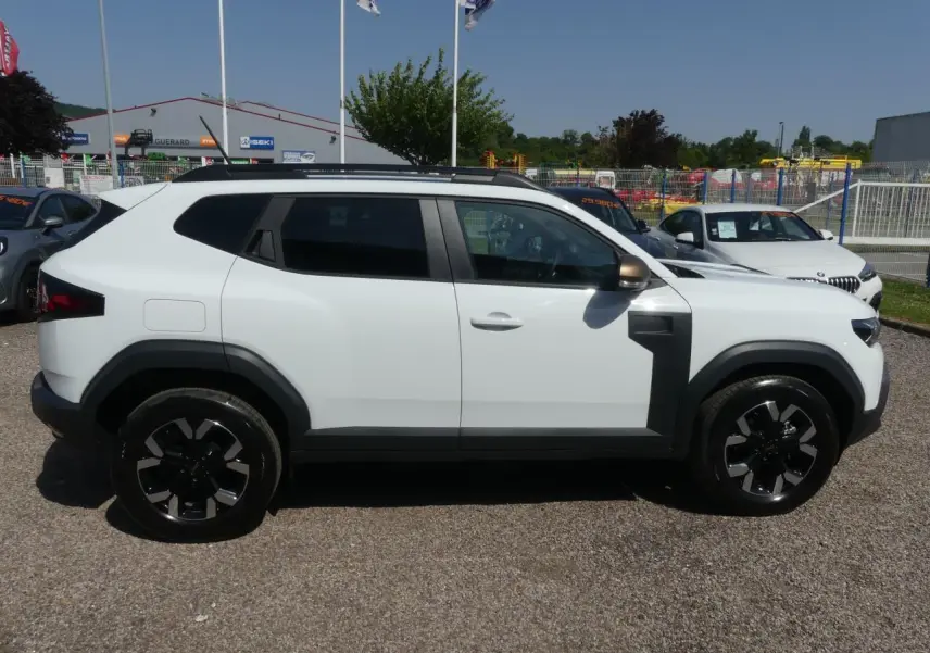 Profil côté gauche du Dacia Duster blanc Glacier 2025 avec jantes alliage noires et détails noirs contrastants.