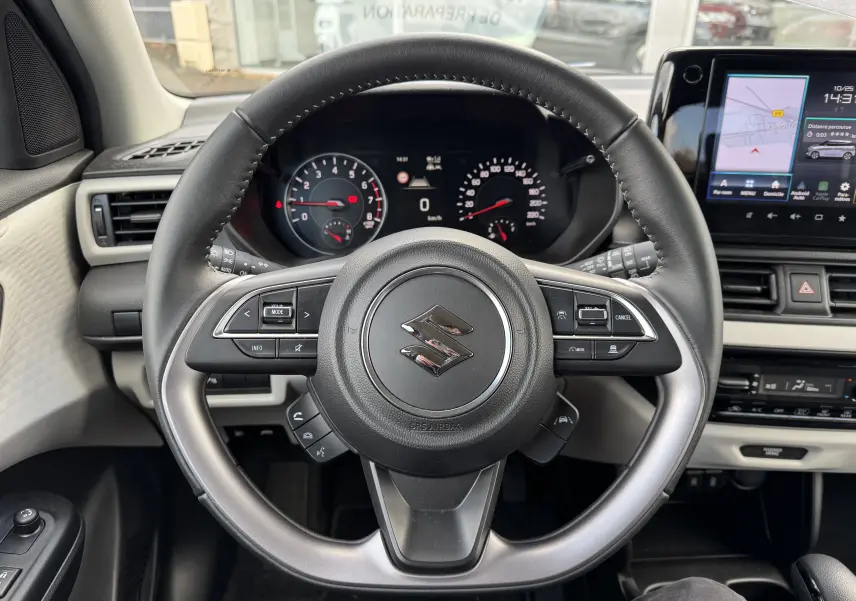 Vue intérieure centrée sur le volant noir de la Suzuki Swift 1.2 Hybrid Privilege, avec tableau de bord et écran tactile visibles.