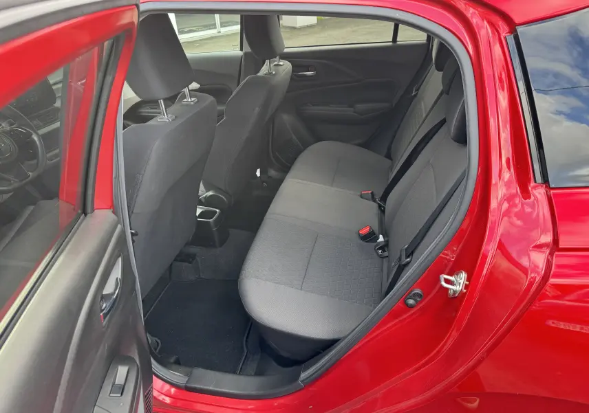 Vue intérieure arrière côté gauche d'une Suzuki Swift 1.2 Hybrid Privilege 2025 rouge Burning Pearl, sièges tissu gris.