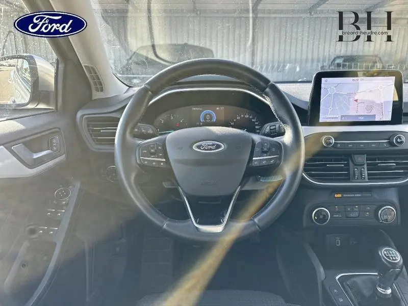 Vue intérieure frontale du poste de conduite d'une Ford Focus 2020 gris lunaire, volant cuir multifonction et écran tactile GPS visible.