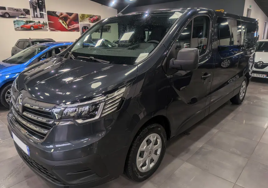 Vue 3/4 avant d'un Renault Trafic Combi L2 gris Comète 2023, avec calandre chromée et jantes acier en showroom.