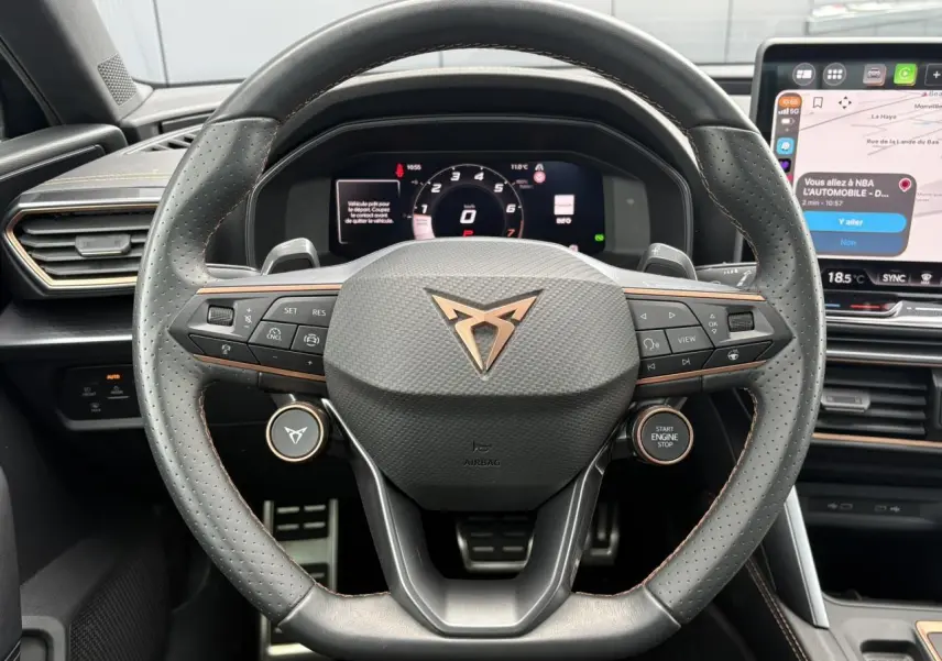 Vue rapprochée du volant cuir perforé noir avec logo CUPRA cuivré et tableau de bord digital d'une Leon 2025.