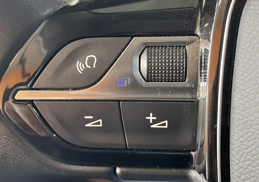 Gros plan sur les commandes au volant noir de la Peugeot 508 gris platinium, avec boutons de volume et activation vocale.