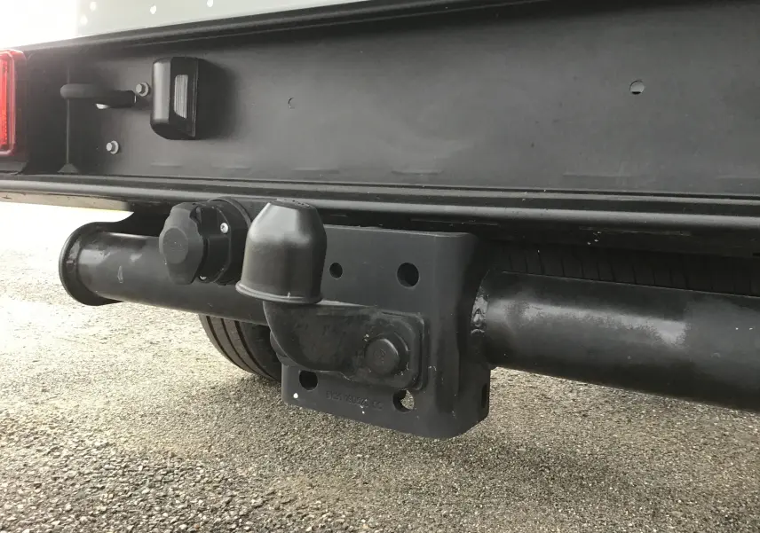 Gros plan sur l'attelage noir sous la benne arrière d'un Ford Transit Châssis Cabine blanc, vue côté gauche.