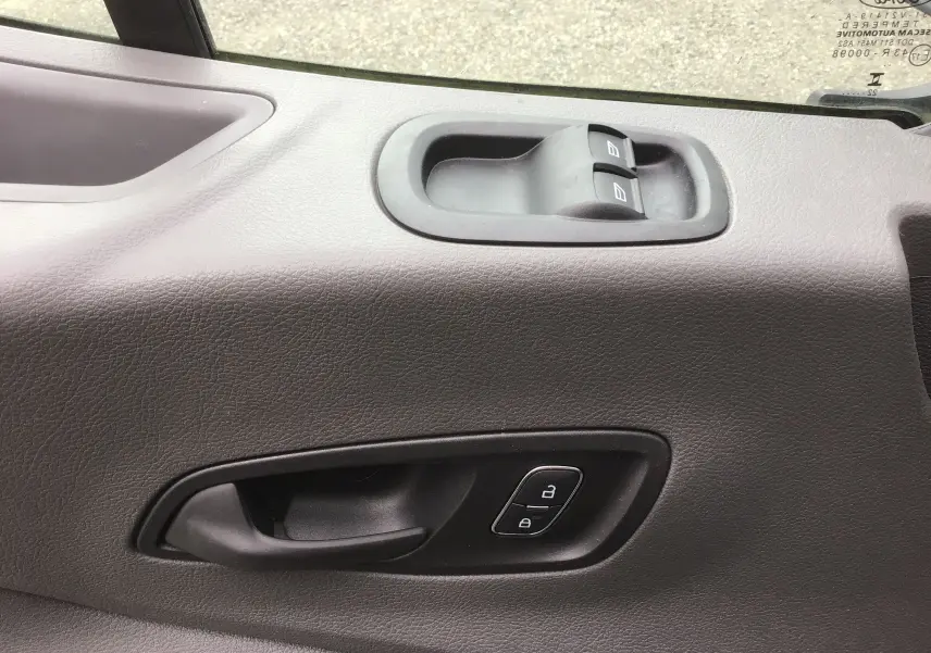 Gros plan sur la poignée intérieure et les commandes de lève-vitres côté conducteur d'un Ford Transit blanc 2024.