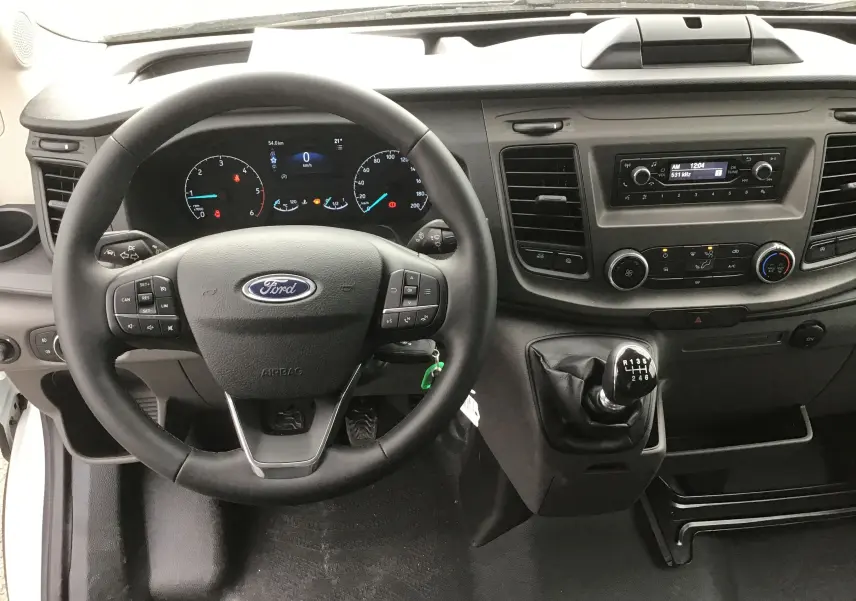 Vue intérieure frontale du poste de conduite du Ford Transit Châssis Cabine blanc, avec volant multifonction et levier de vitesses manuel.