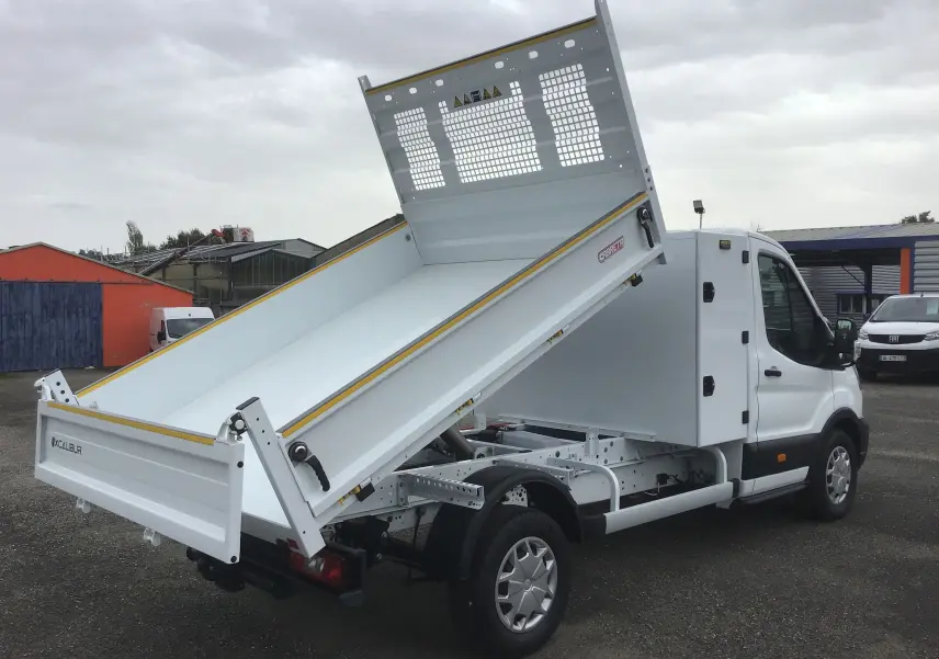 Ford Transit Chassis Cabine blanc vu de trois quarts arrière droit, avec benne Cabreta relevée et coffre intégré.