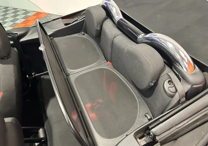 Vue plongeante sur l'intérieur arrière d'une MINI Cabriolet rouge, montrant les appuie-têtes et l'arceau chromé de sécurité.