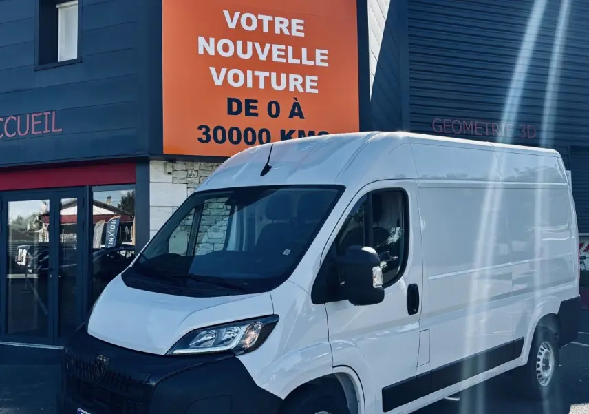 PEUGEOT Boxer Fourgon blanc vu en 3/4 avant droit devant un bâtiment commercial avec panneau orange.