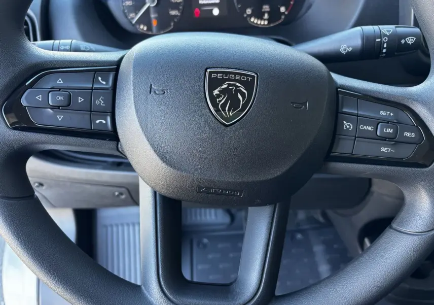 Gros plan sur le volant noir multifonctions du Peugeot Boxer Fourgon 2025, avec logo lion central visible.