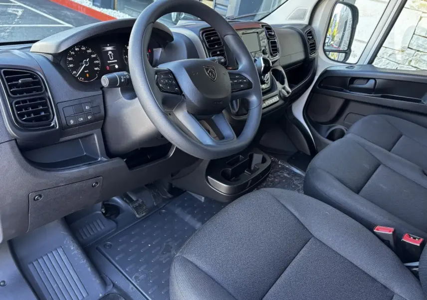 Intérieur du Peugeot Boxer Fourgon 2025 vu côté conducteur, tableau de bord noir avec volant multifonction et sièges gris.