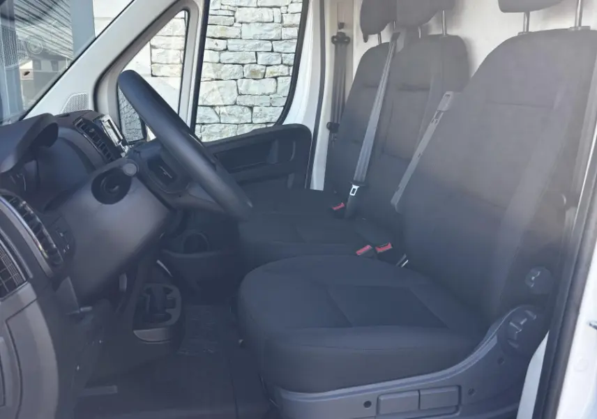 Vue intérieure côté conducteur du Peugeot Boxer Fourgon blanc 2025, montrant les sièges noirs et le tableau de bord.