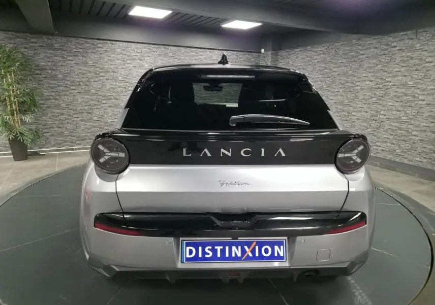 Vue arrière d'une Lancia Ypsilon gris bi-color avec toit noir et feux ronds distinctifs dans un showroom.