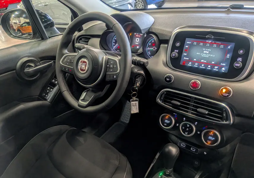 Vue intérieure côté conducteur de la Fiat 500X 2024 noire, avec tableau de bord numérique et écran tactile central allumé.