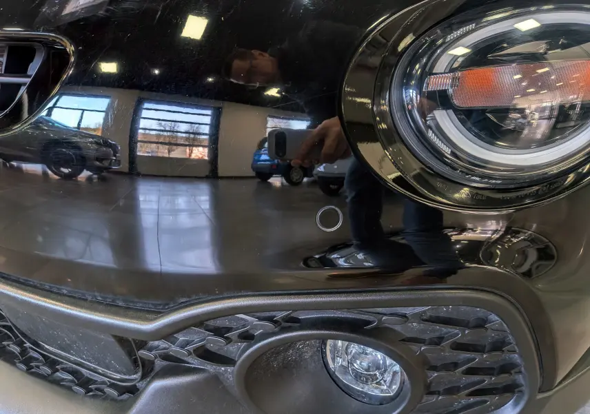 Gros plan sur le phare avant droit et la calandre d'une FIAT 500X 2024 en noir cinéma avec finition brillante.