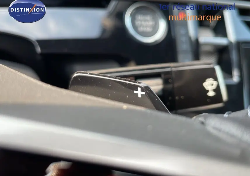 Gros plan sur la palette de changement de vitesse + au volant d’un Peugeot 3008 gris Artense, intérieur moderne et lumineux.