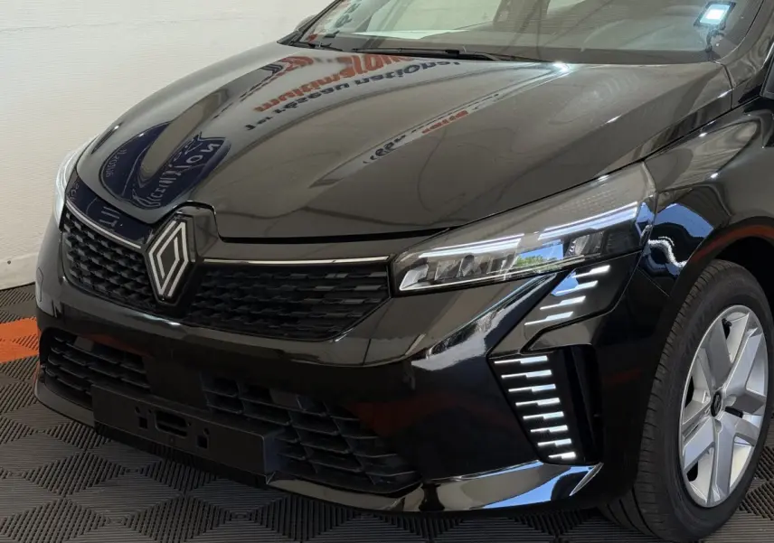 Vue 3/4 avant droit d'une Renault Clio noire 2025 avec phares LED et calandre au logo Renault proéminent.