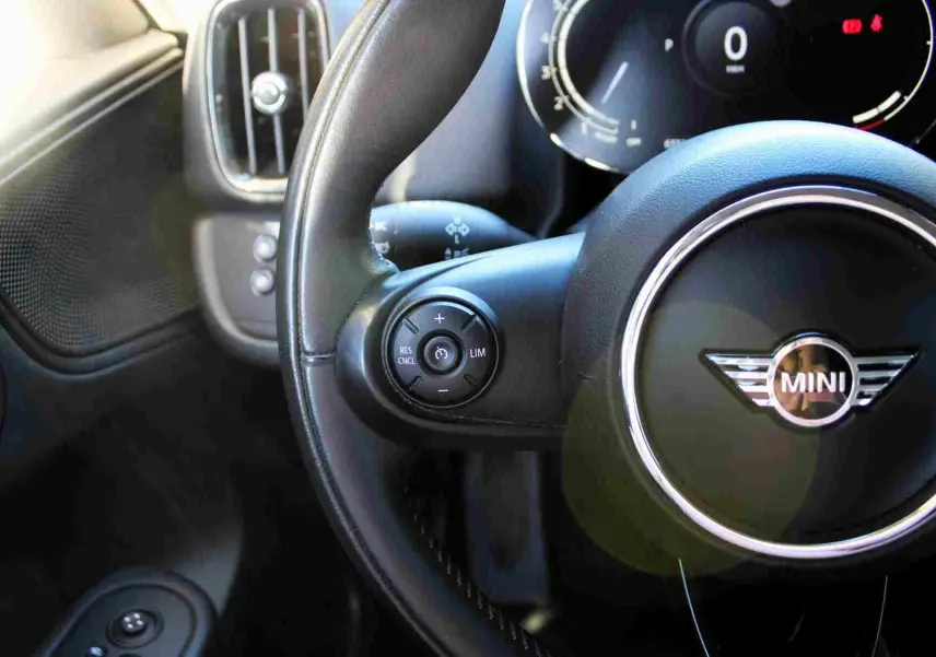 Gros plan sur le volant cuir noir de la MINI Countryman II avec commandes intégrées et tableau de bord digital en arrière-plan.