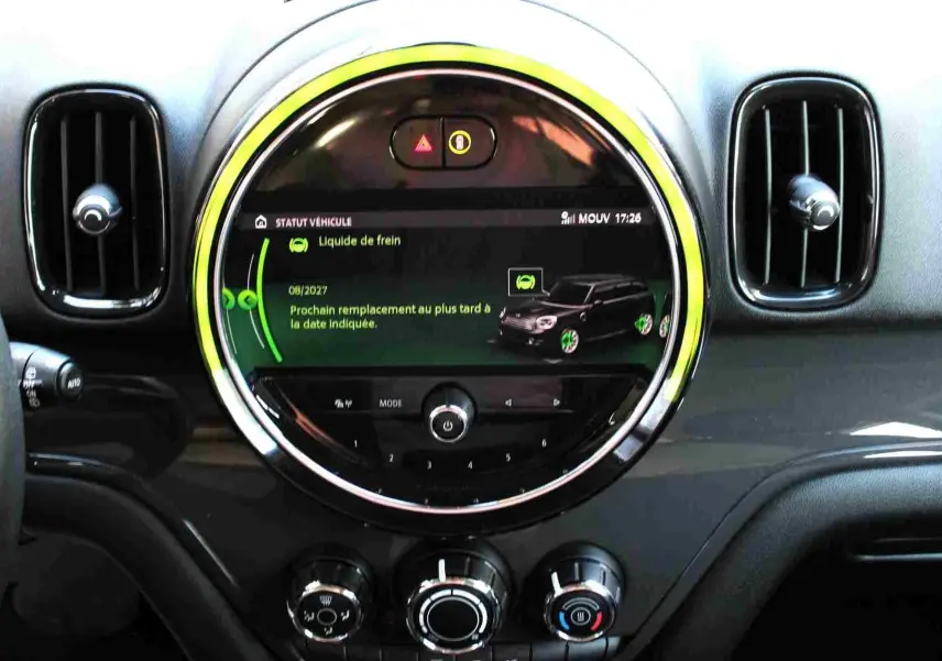 Vue rapprochée du tableau de bord de la MINI Countryman 2020, écran central rond avec affichage d'entretien et aérateurs noirs.