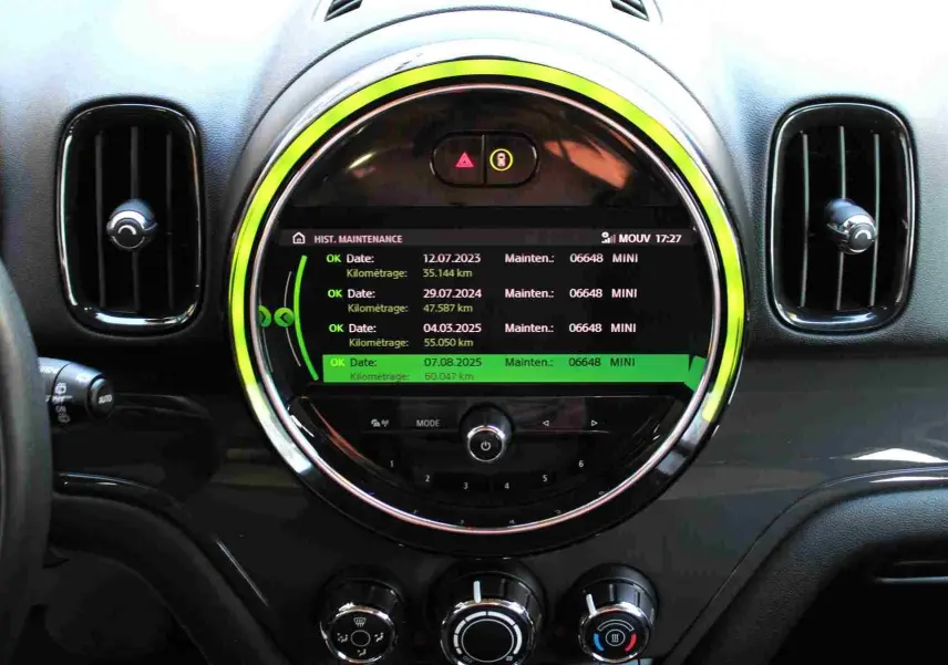 Vue rapprochée du tableau de bord central noir du MINI Countryman avec écran rond affichant l'historique de maintenance.