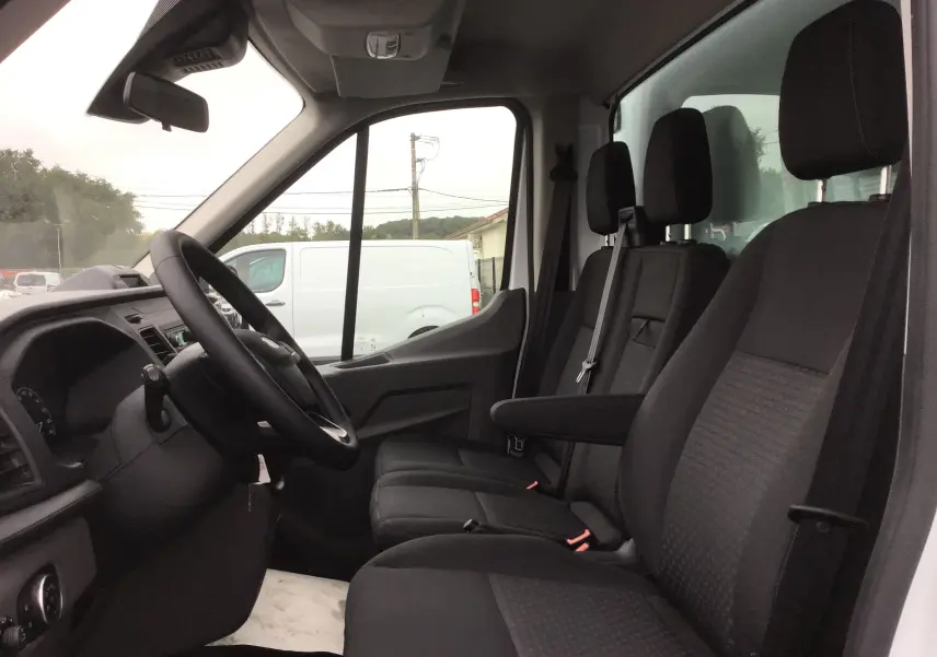 Vue intérieure côté conducteur du Ford Transit Chassis Cabine blanc 2024 avec sièges noirs et tableau de bord simple.