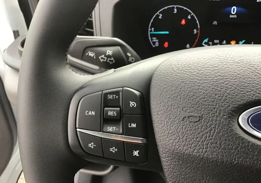 Gros plan sur le volant noir du Ford Transit blanc, mettant en valeur les commandes de régulateur de vitesse et volume sonore.