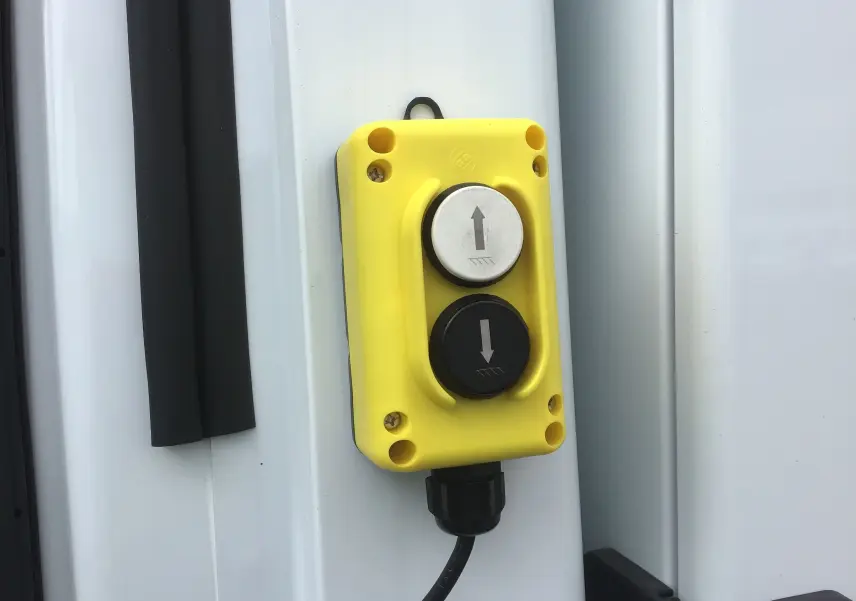 Gros plan sur commande jaune de levage avec boutons fléchés montée sur la benne blanche d'un Ford Transit Châssis Cabine.
