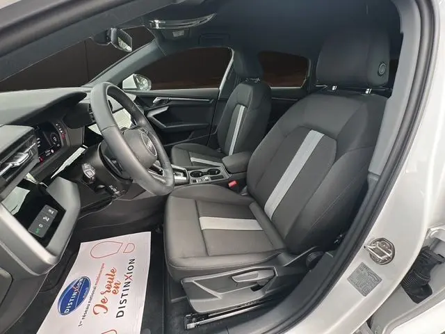 Vue intérieure côté conducteur de l'Audi A3 Sportback 2024 blanc Arkona, sièges tissu noir avec bande grise centrale.