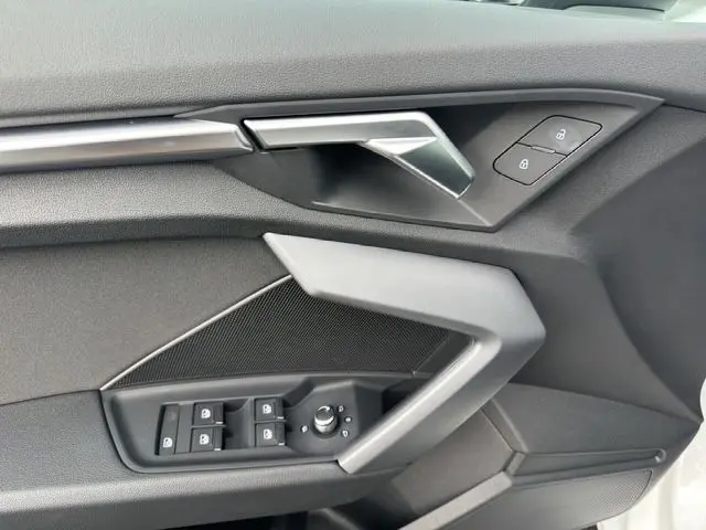 Détail de la porte intérieure côté conducteur de l’Audi A3 Sportback 2024 en tissu noir avec commandes électriques et poignée argentée.
