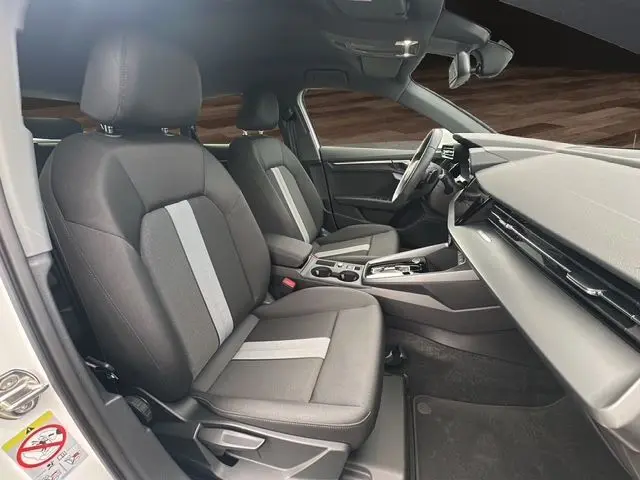 Vue intérieure côté conducteur de l'Audi A3 Sportback 2024 avec sièges tissu noir et bande grise centrale.